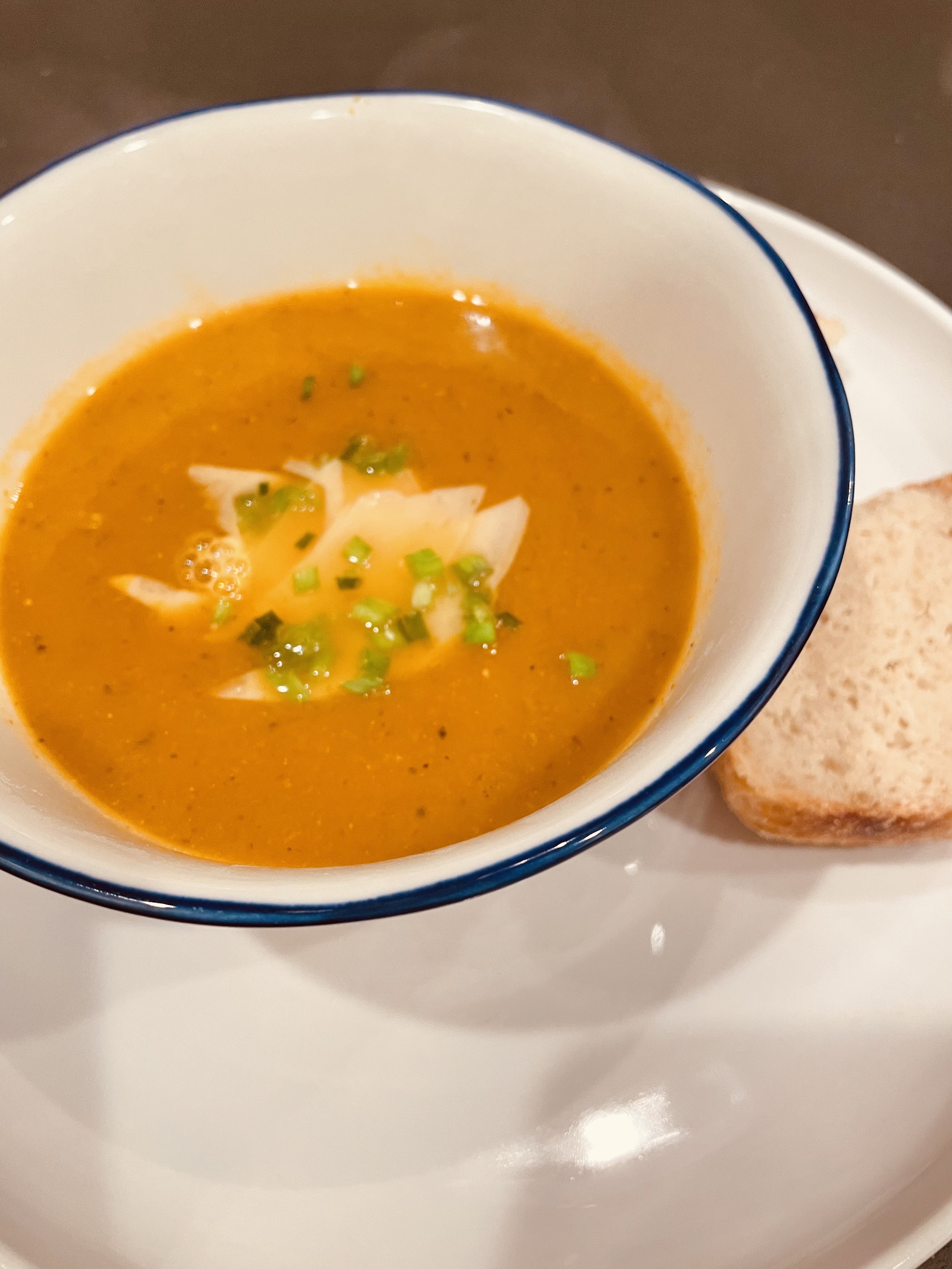 A bowl of carrot soup, topped with chives and grated Parmesan cheese, alongside some crusty homemade bread