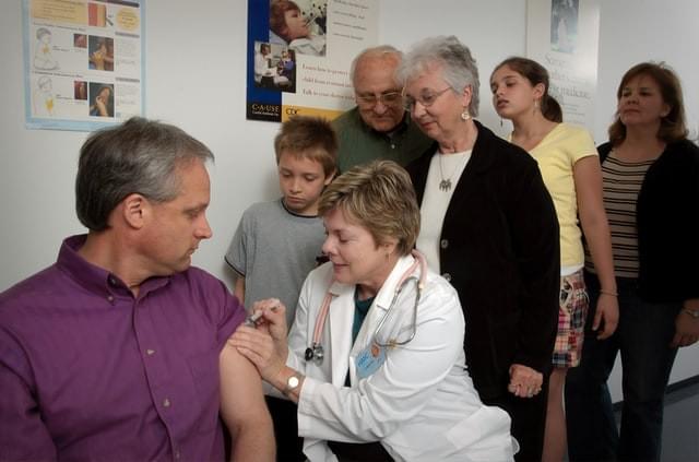 A man receiving a vaccine while a multigenerational family watches